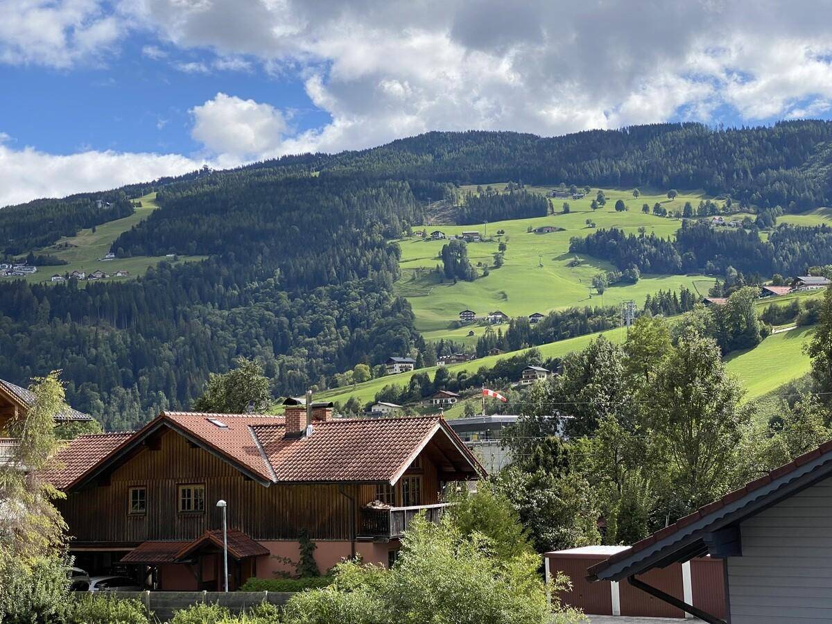 Malerischer Blick auf die grüne Berglandschaft mit traditionellen Häusern unter blauem Himmel.