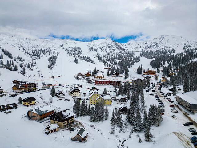 Weitläufige Luftaufnahme des verschneiten Dorfes in einer beeindruckenden Berglandschaft im Winter.