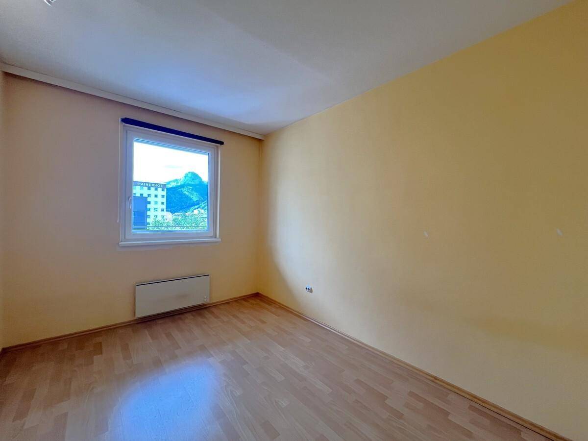 Leeres Schlafzimmer mit hellem Laminatboden und einem Fenster, das Tageslicht hereinlässt.