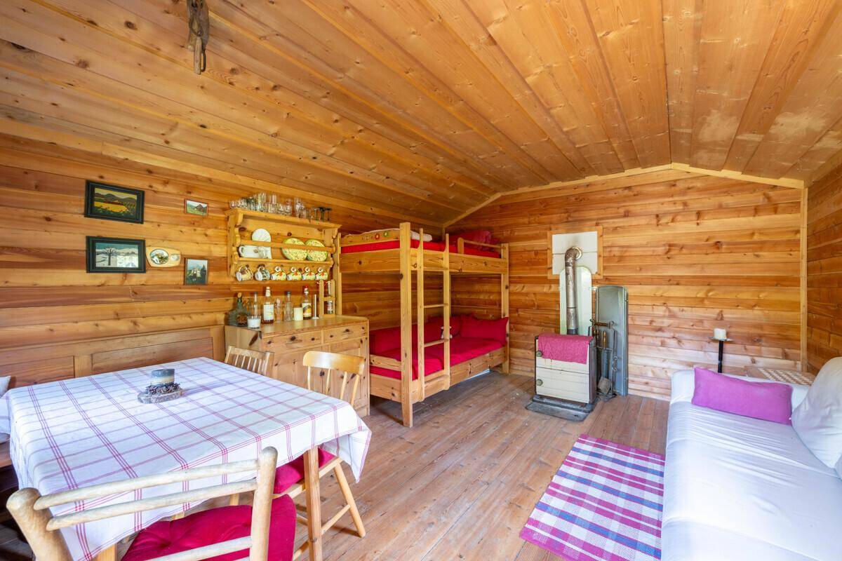 Gemütlicher Wohn-Essbereich in einer Holzhütte mit Etagenbetten, Sofa und Holzofen.
