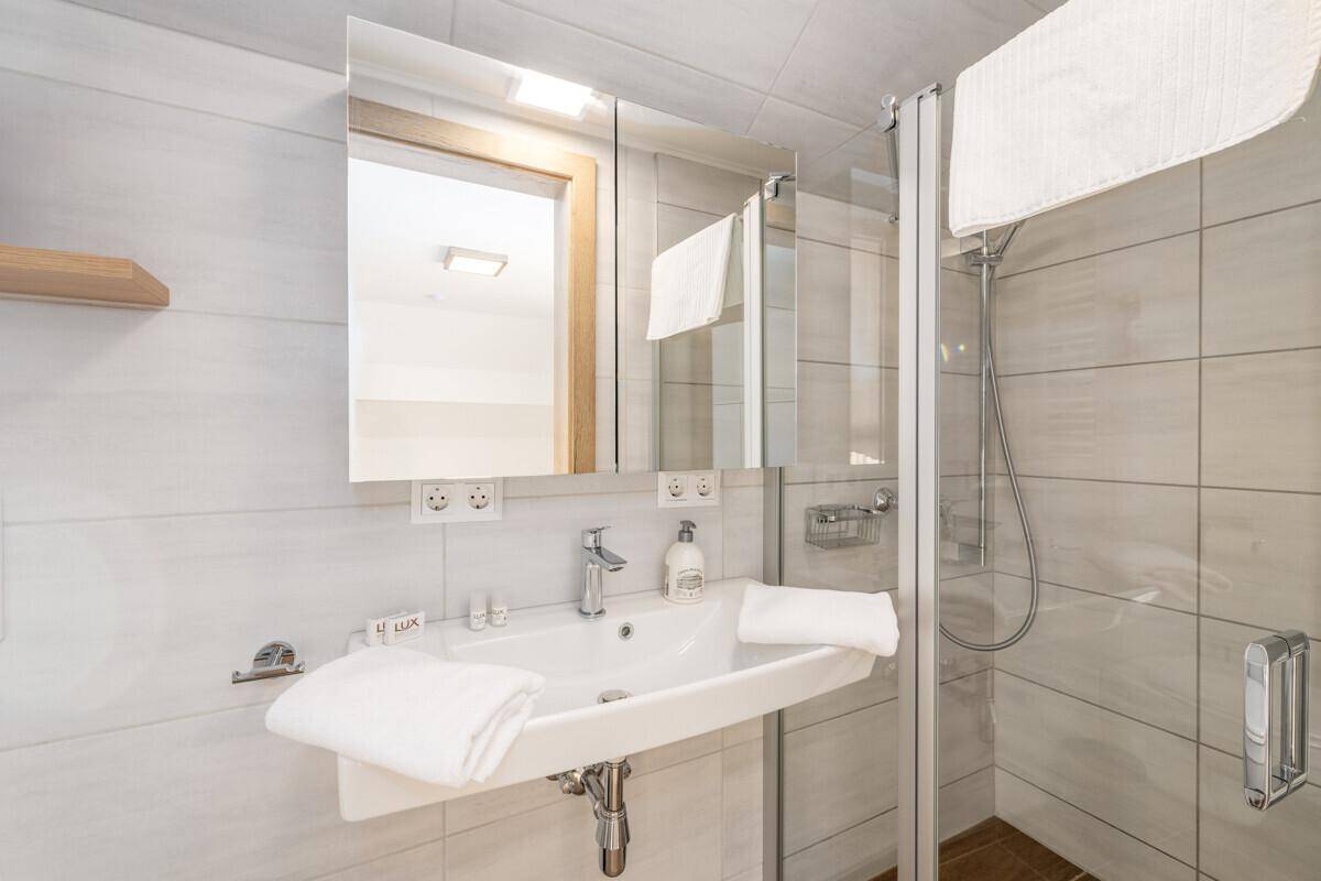 Helles Badezimmer mit Waschbecken, Spiegel und Duschkabine, modern gefliest.