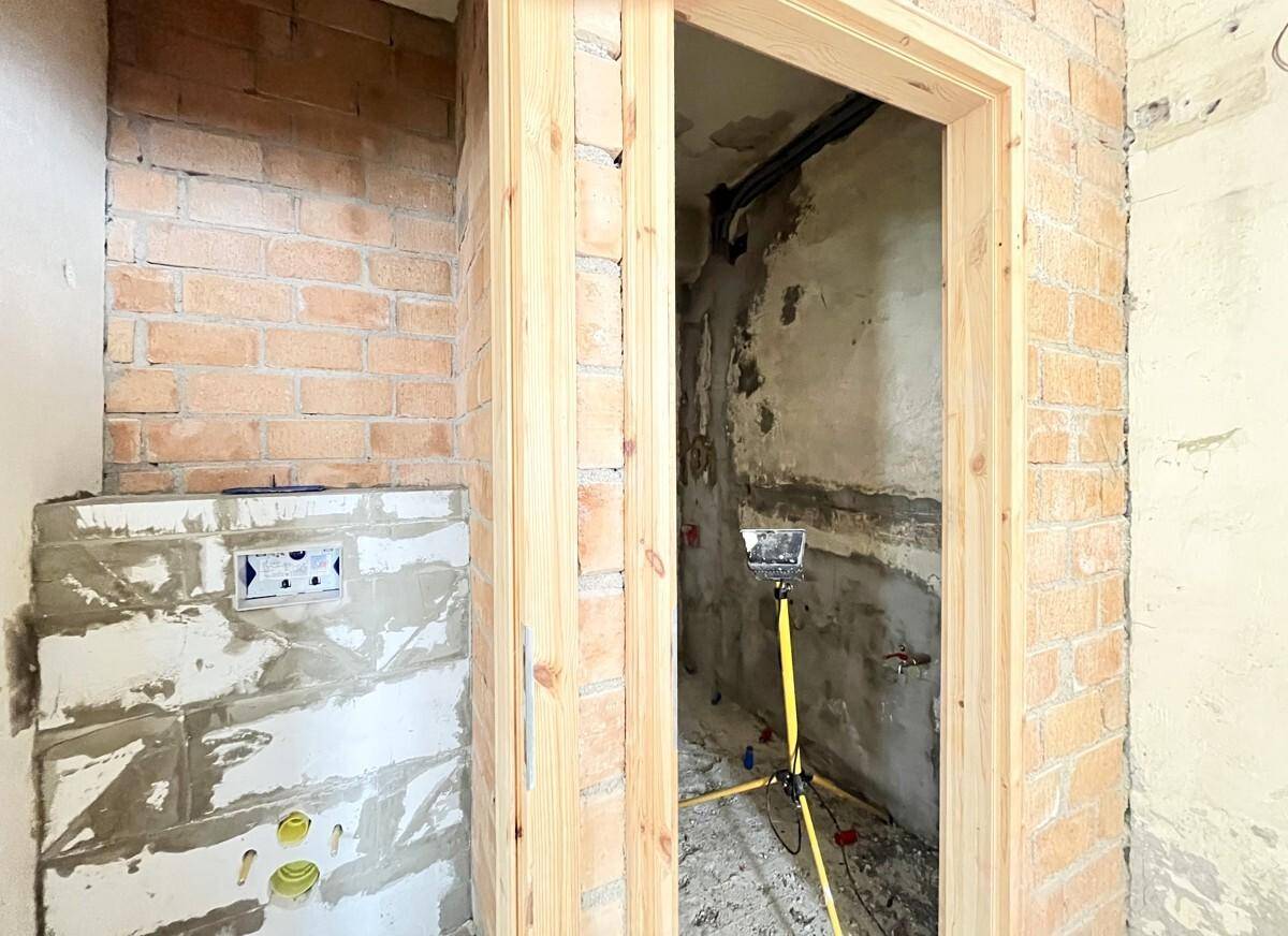 Badezimmer oder WC im Rohbau mit sichtbaren Ziegelwänden und Installationen.
