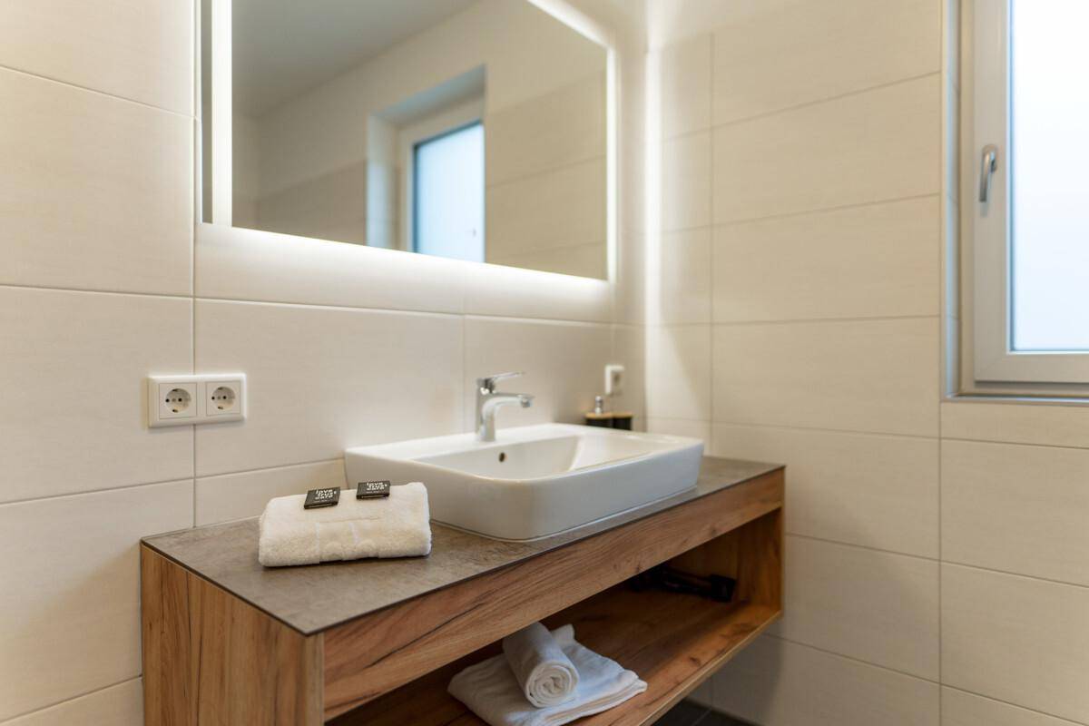 Modernes Badezimmer mit Einzelwaschbecken, beleuchtetem Spiegel und großen Fliesen.