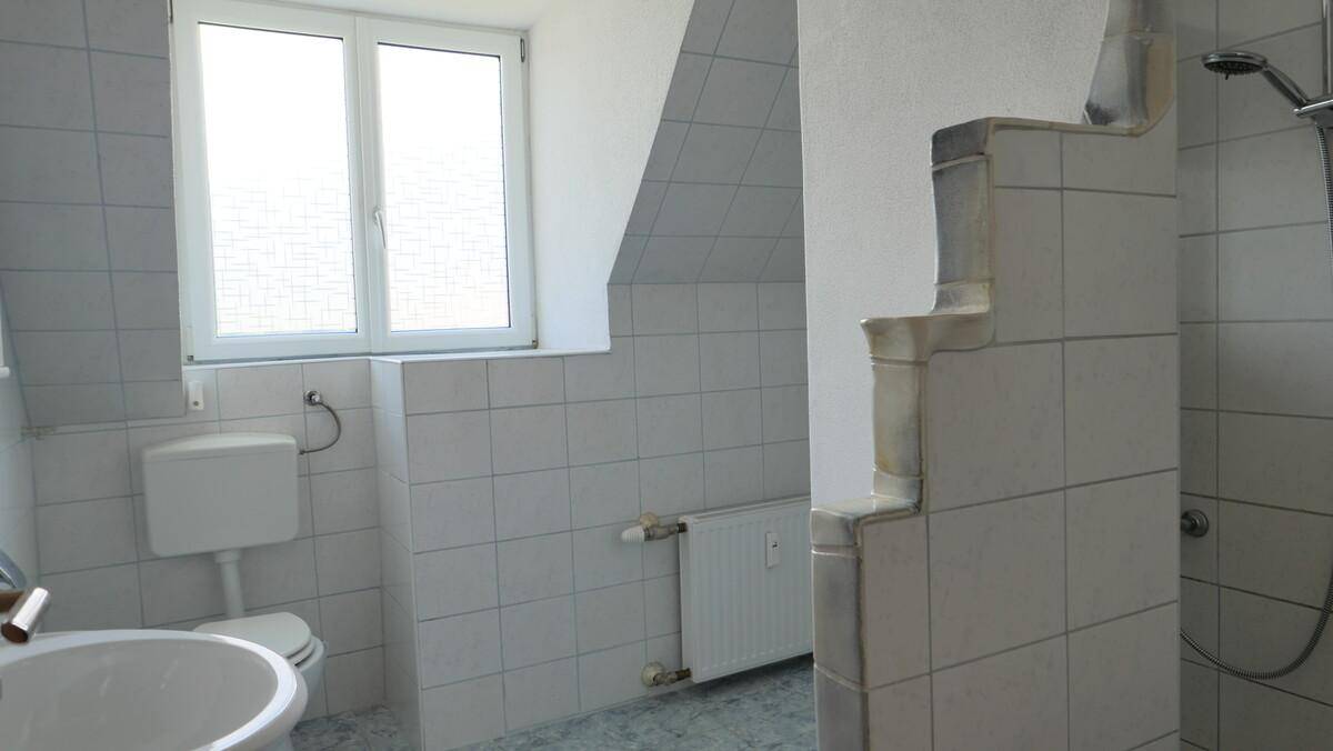 Gefliestes Badezimmer mit Dusche, WC und Fenster unter der Dachschräge.