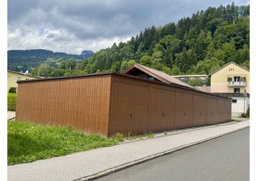 Lange, braune Holzfassade eines Gebäudes mit bewaldeten Hügeln im Hintergrund.