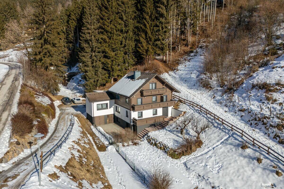 Idyllisches Haus in alpiner Landschaft, umgeben von Wald und Schnee, mit Zufahrt.