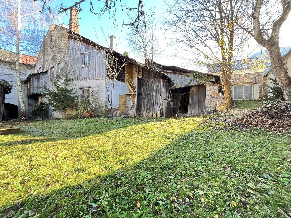 Großer, sonniger Gartenbereich mit Rasen und alten Gebäuden im Hintergrund, umgeben von Bäumen.