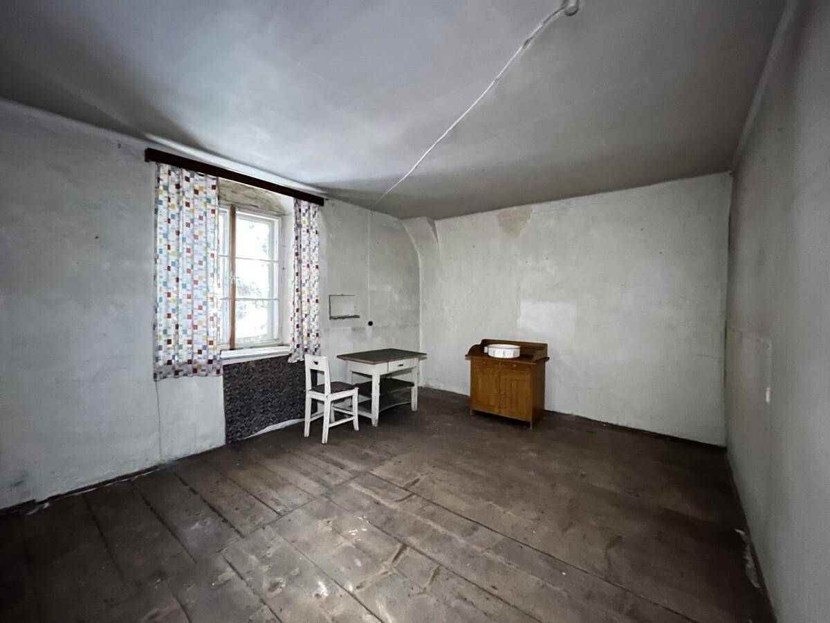 Einfacher Raum mit Holzdielenboden, einem Fenster mit Vorhängen und einigen alten Möbelstücken.