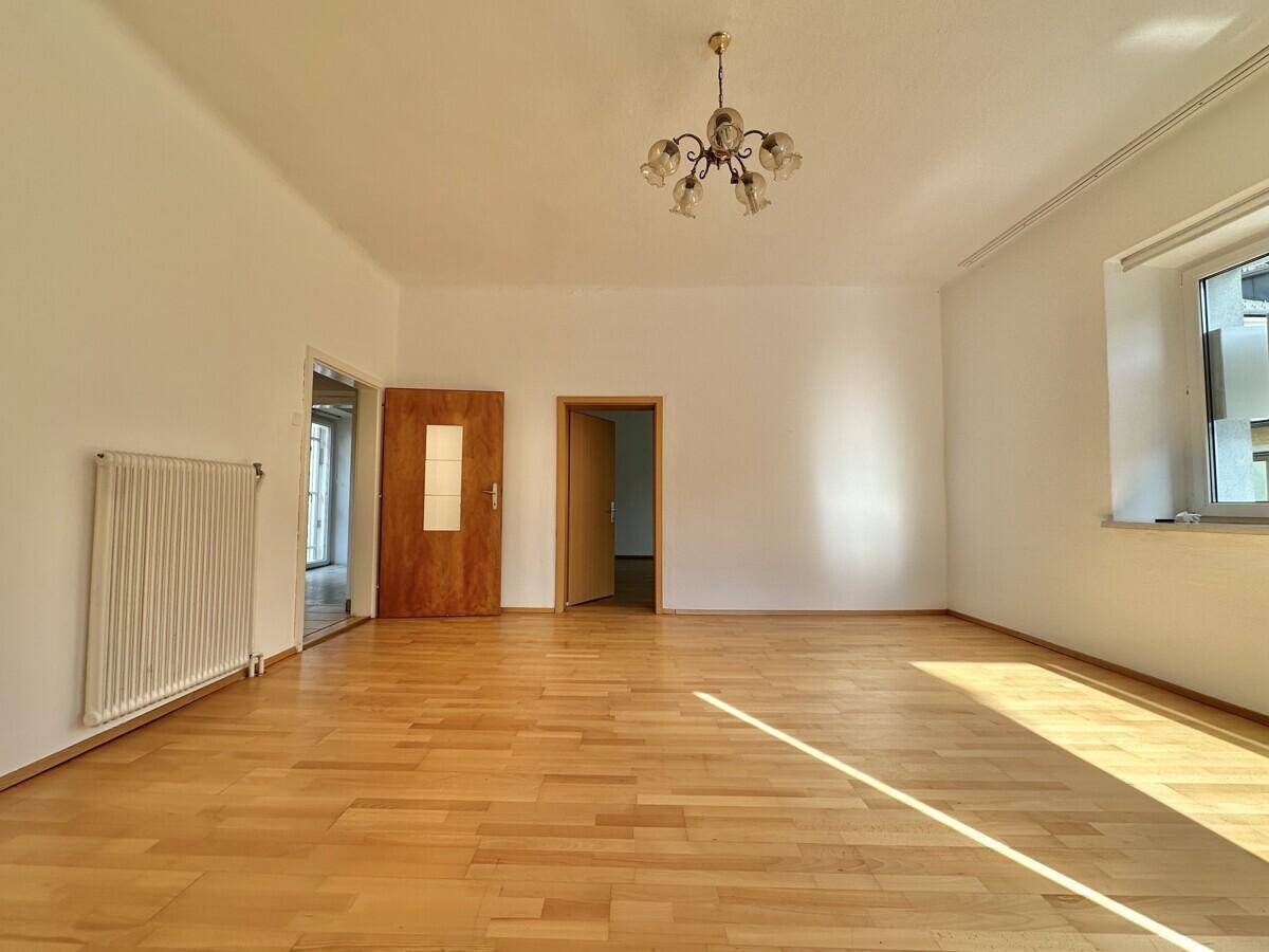 Geräumiger, heller Raum mit Parkettboden, Heizkörper und Kronleuchter, bereit zur Einrichtung.