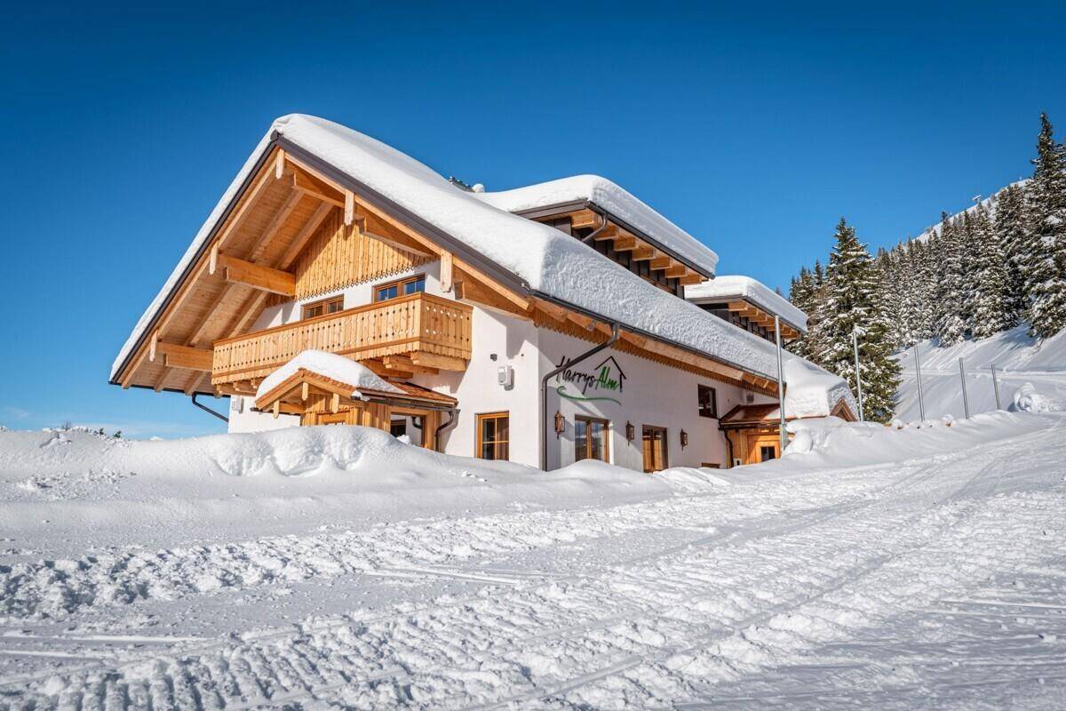 Traditionelles Alpenhaus mit Holzbalkonen und schneebedecktem Dach unter blauem Himmel.