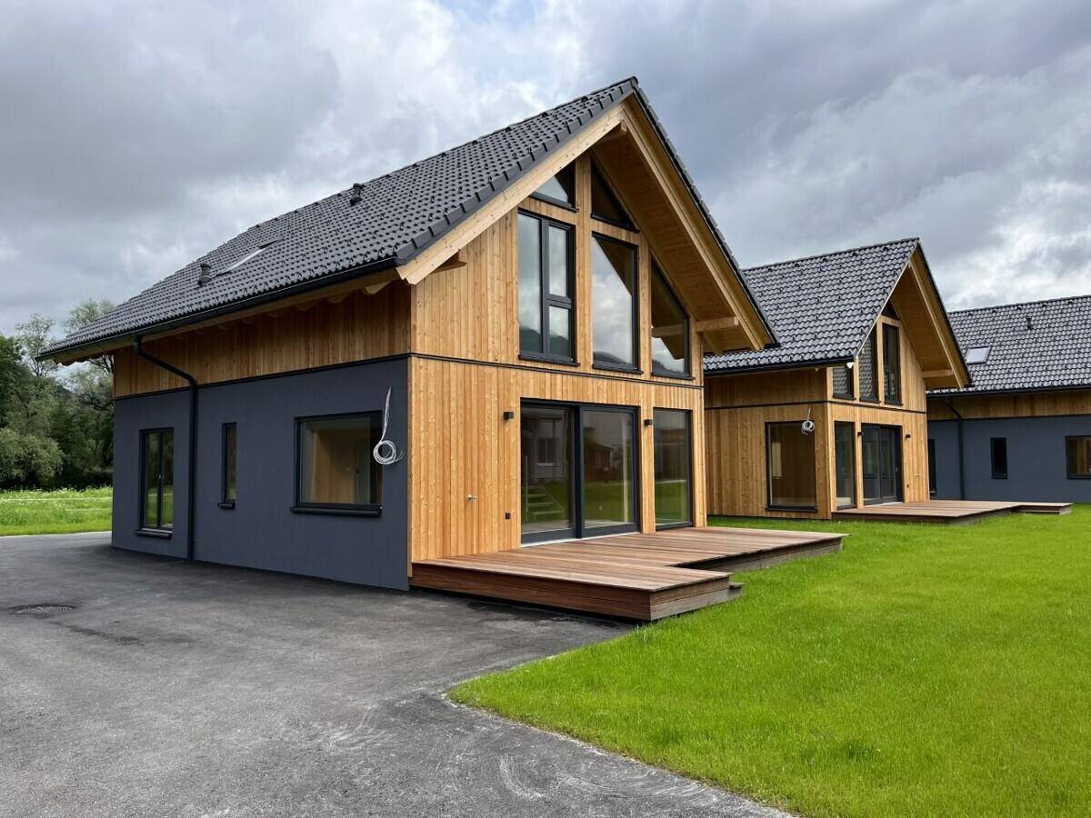 Zwei moderne Häuser mit Holzterrassen, großen Fenstern und gepflegtem Rasenbereich.