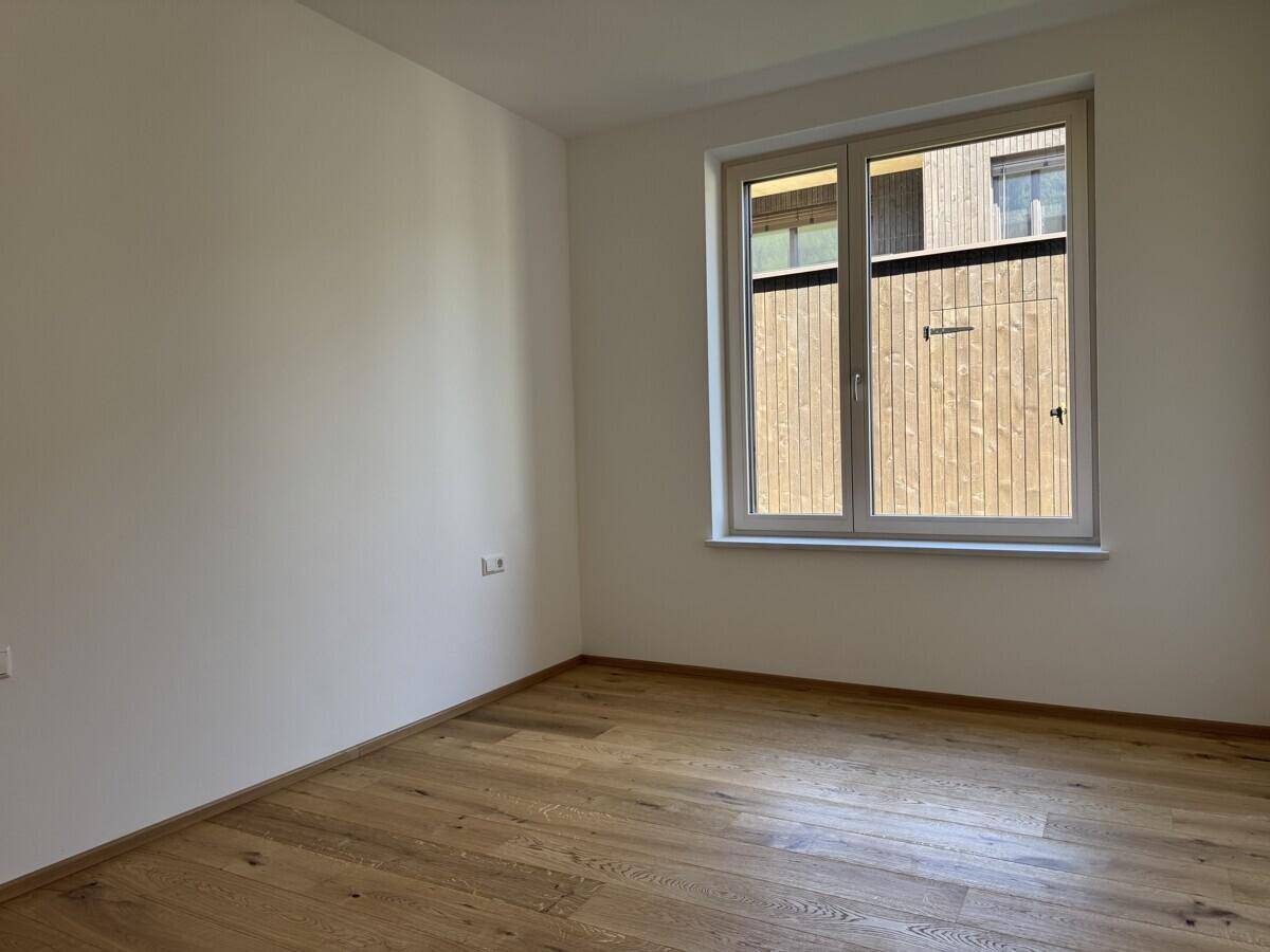 Leeres Zimmer mit hellem Holzfußboden und einem Fenster, das Licht in den Raum bringt.