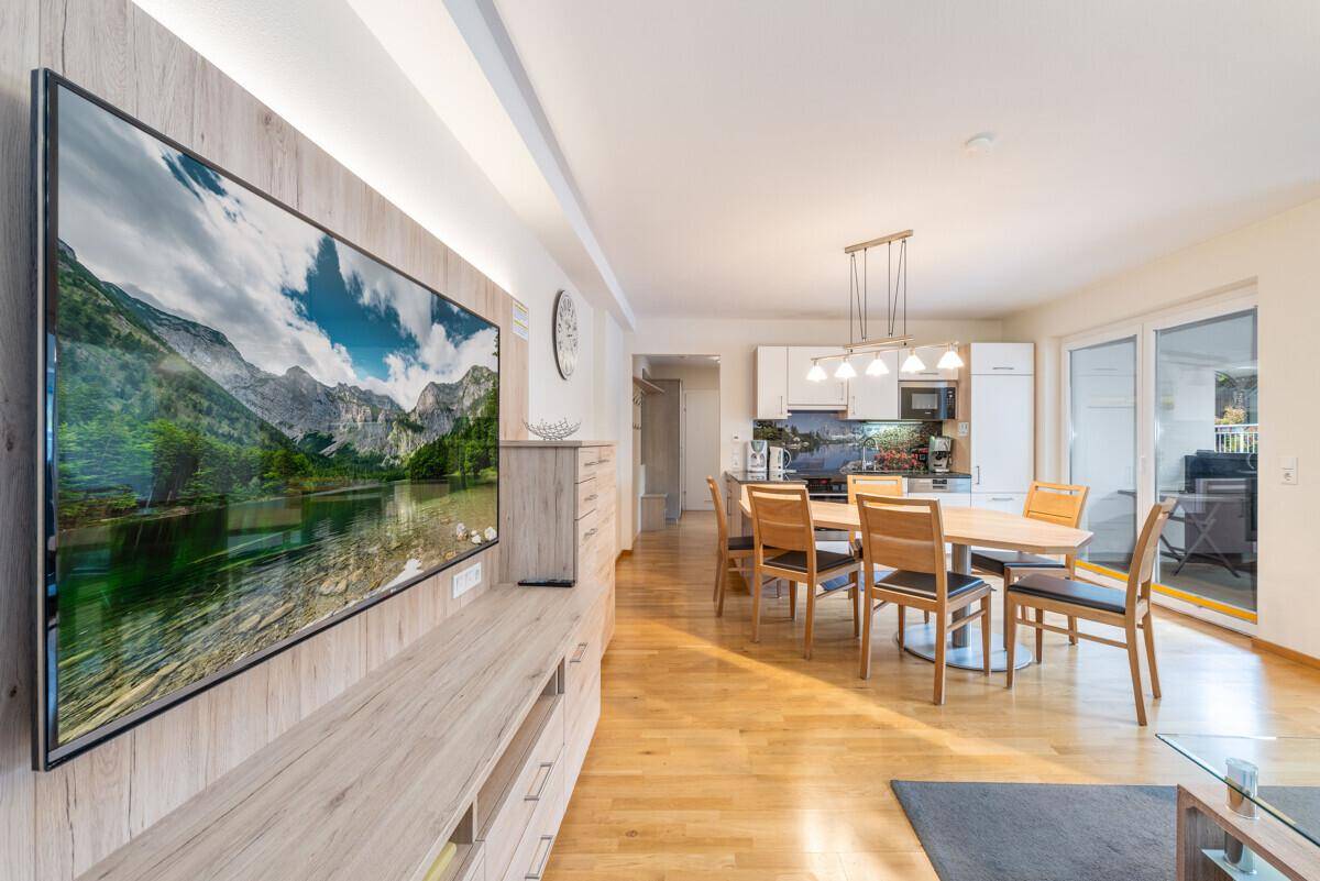 Moderner Wohnbereich mit großem Wandfernseher und Holzmöbeln, angrenzend an den Essbereich.