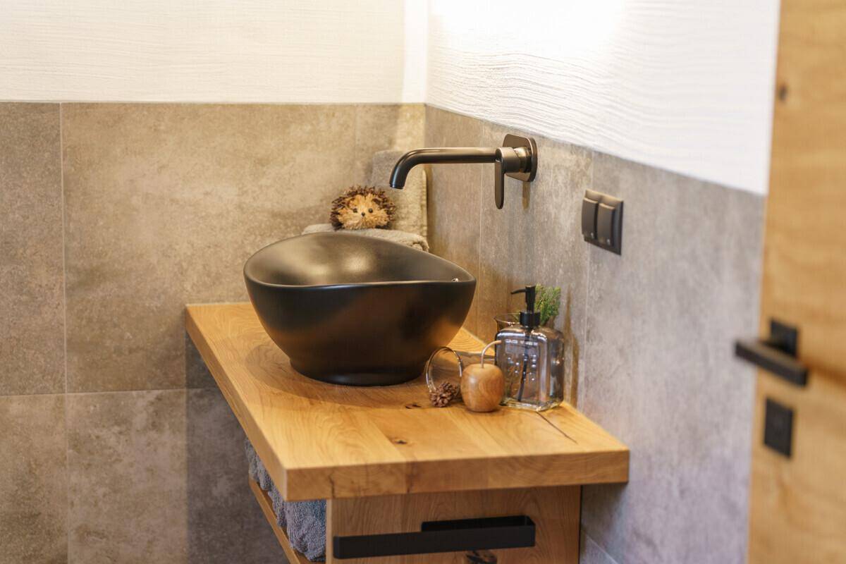 Modernes Gäste-WC mit schwarzem Aufsatzwaschbecken und Holztischplatte.