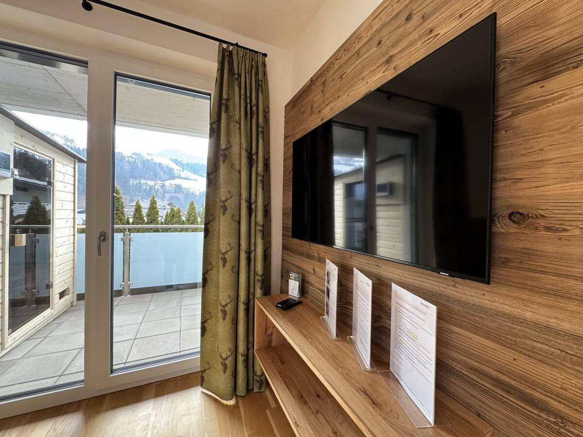 Detailansicht des Fernsehbereichs mit Holzwand und Zugang zum Balkon.