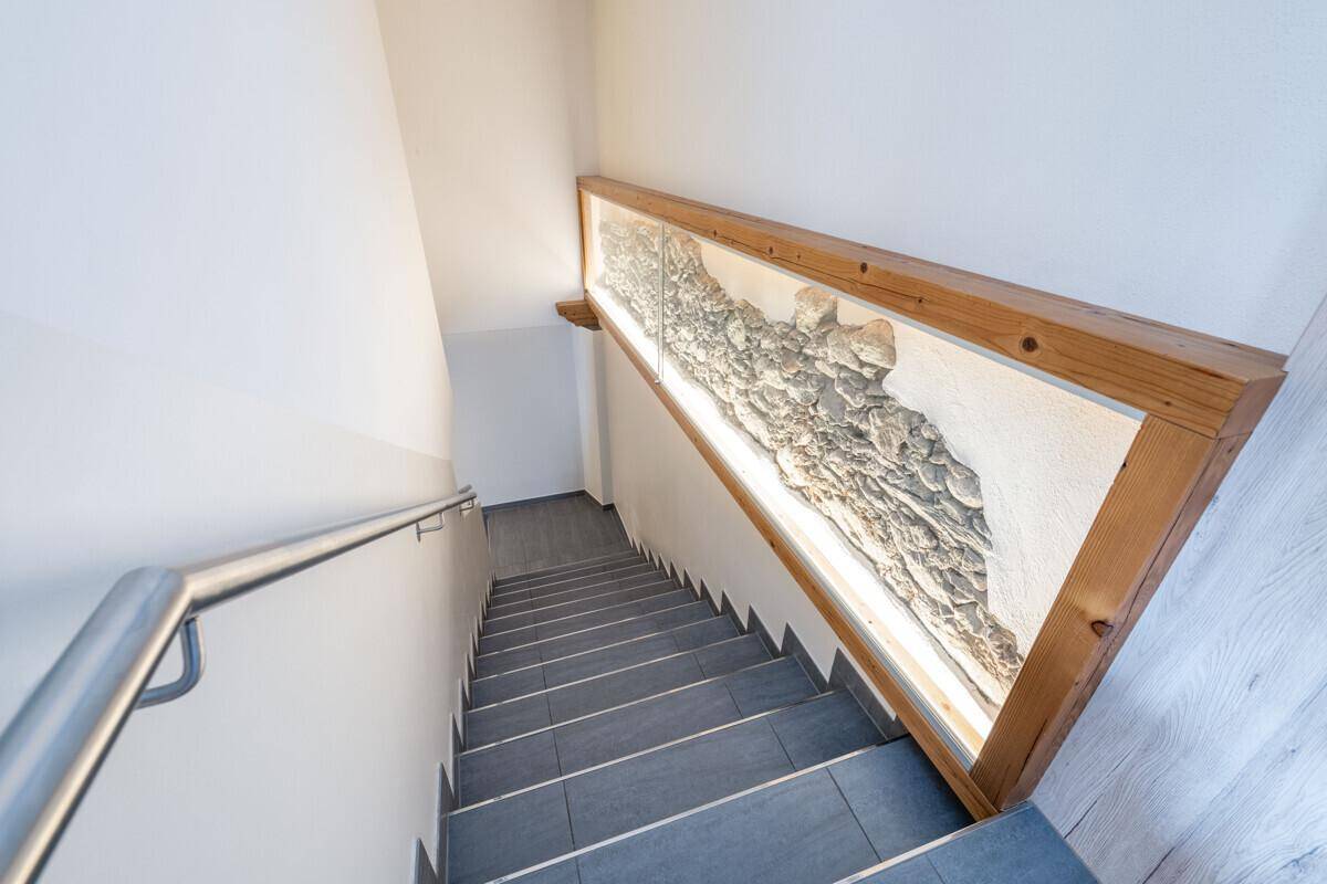 Treppenhaus mit modernen Fliesenstufen und einem dekorativen Wandelement aus Naturstein.