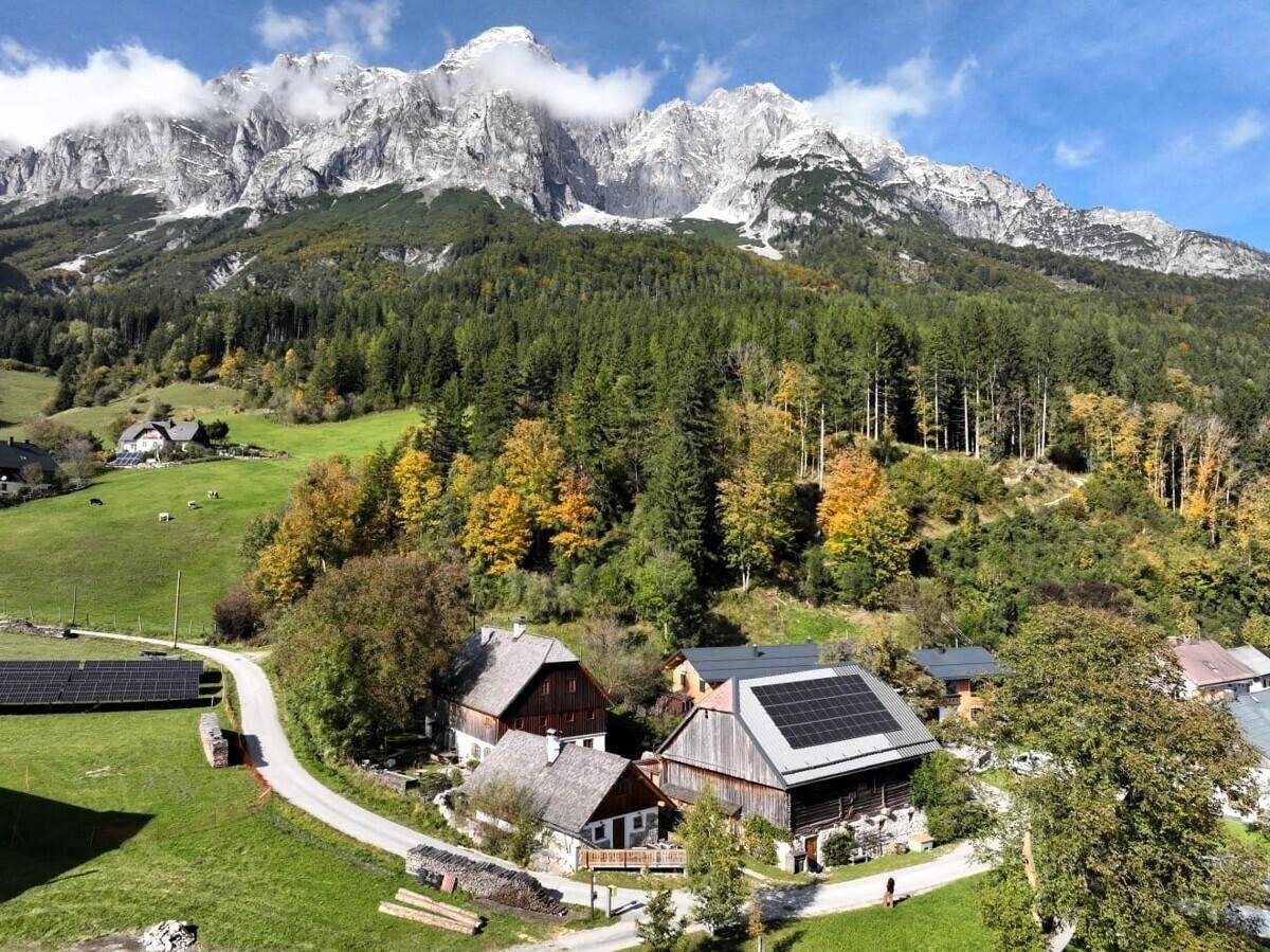 Weitläufige Luftaufnahme einer ländlichen Siedlung vor majestätischer Bergkulisse mit Solaranlagen.