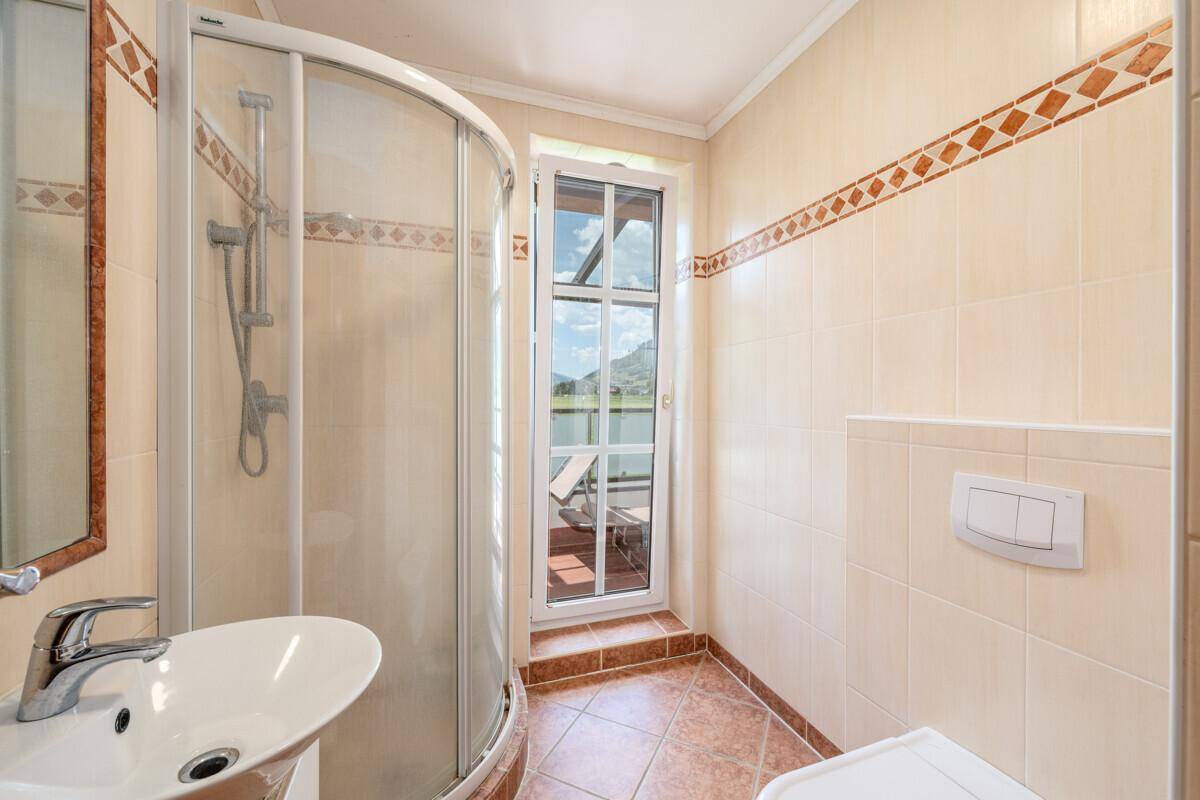 Kleines Badezimmer mit Dusche, WC und Fenster, hell gefliest in warmen Farbtönen.