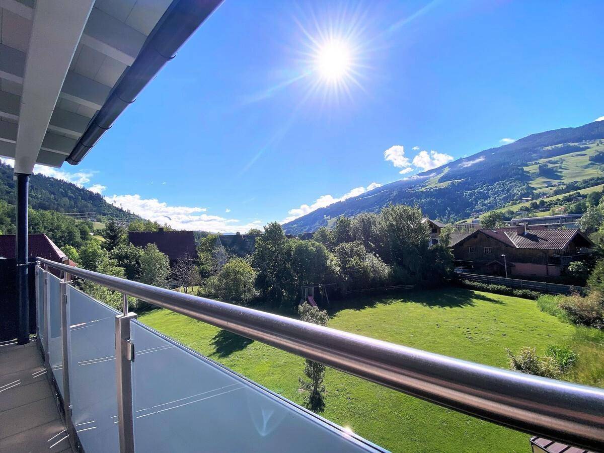 Sonniger Balkon mit Glasgeländer und Panoramablick auf die umliegende Berglandschaft.