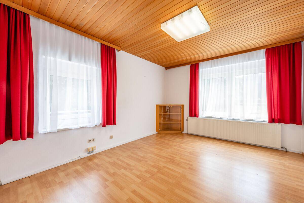 Helles Zimmer mit Holzdecke, Laminatboden und roten Vorhängen, bietet viel Licht.