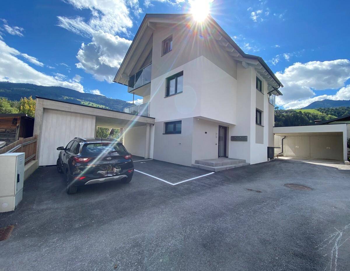 Neubau mit moderner Architektur, Carport und sonnigem Außenbereich vor Bergkulisse.