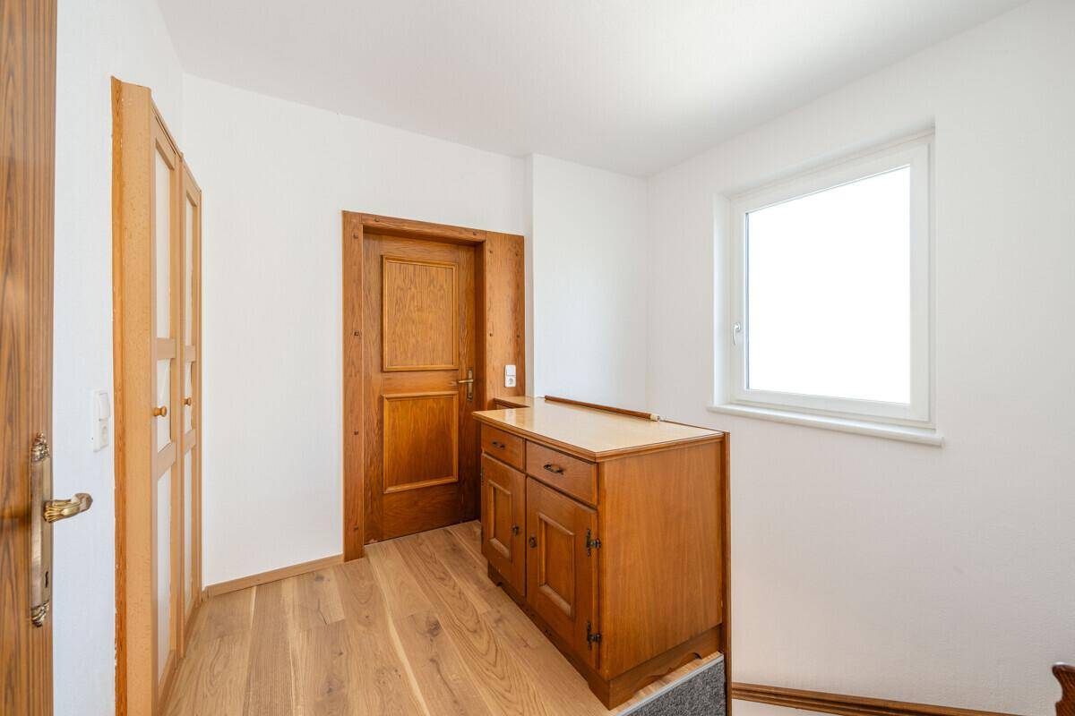 Flur mit Holzboden, Fenster und einem kleinen Holzschrank, der zu einem weiteren Raum führt.