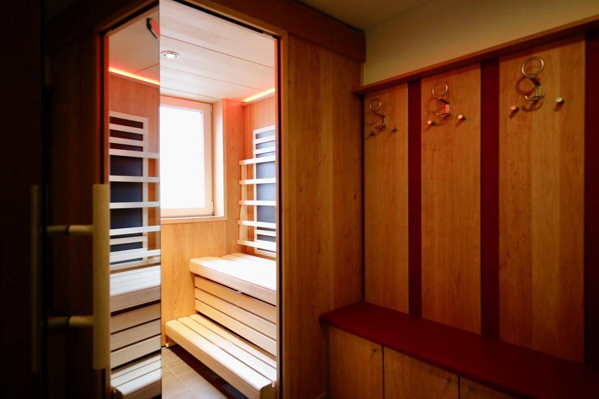 Moderne Sauna mit Holzbänken und einem Fenster, angrenzend an einen Garderobenbereich.