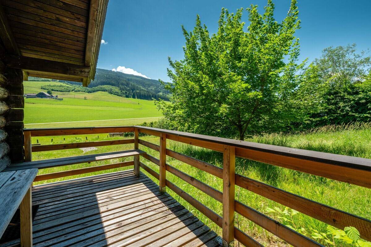 Kleiner Holzbalkon mit Sitzbank und idyllischem Blick auf grüne Wiesen und Berge.