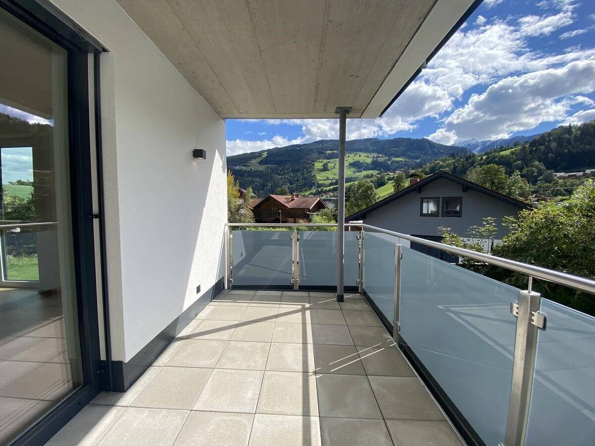 Geräumiger Balkon mit Fliesenboden, Glasgeländer und weitem Blick auf die grüne Berglandschaft.