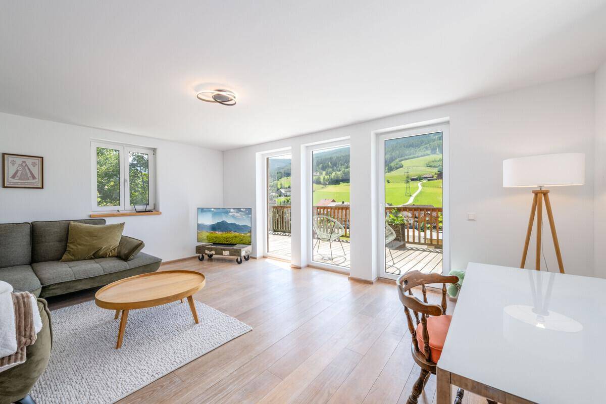 Heller Wohn-Essbereich mit Sofa, Fernseher und Esstisch, mit Zugang zum Balkon.