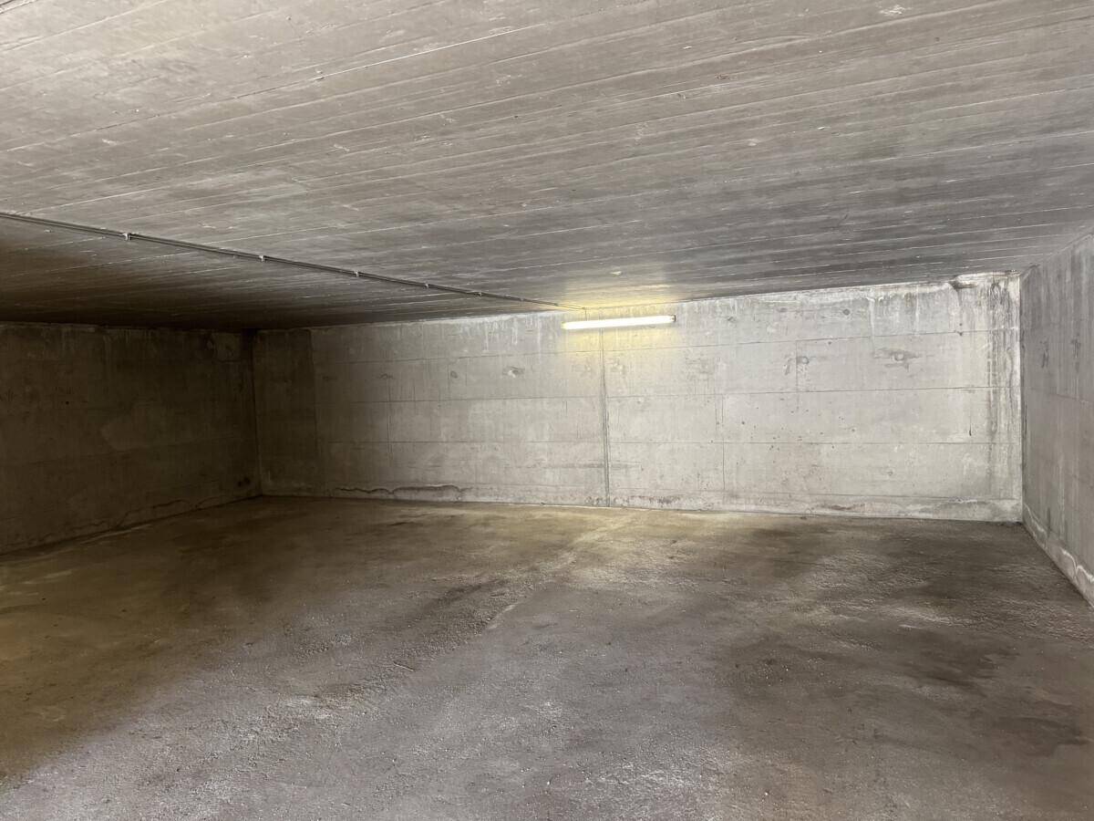 Leere Tiefgarage mit Betonwänden und -boden, beleuchtet von einer einzelnen Leuchte.