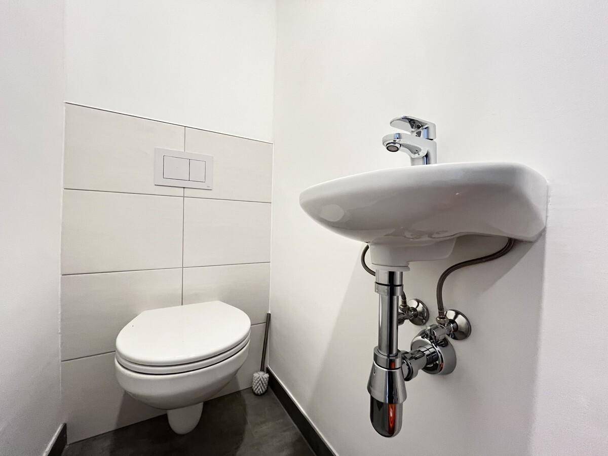 Kleines Gäste-WC mit wandhängender Toilette, kleinem Waschbecken und weißen Wandfliesen.