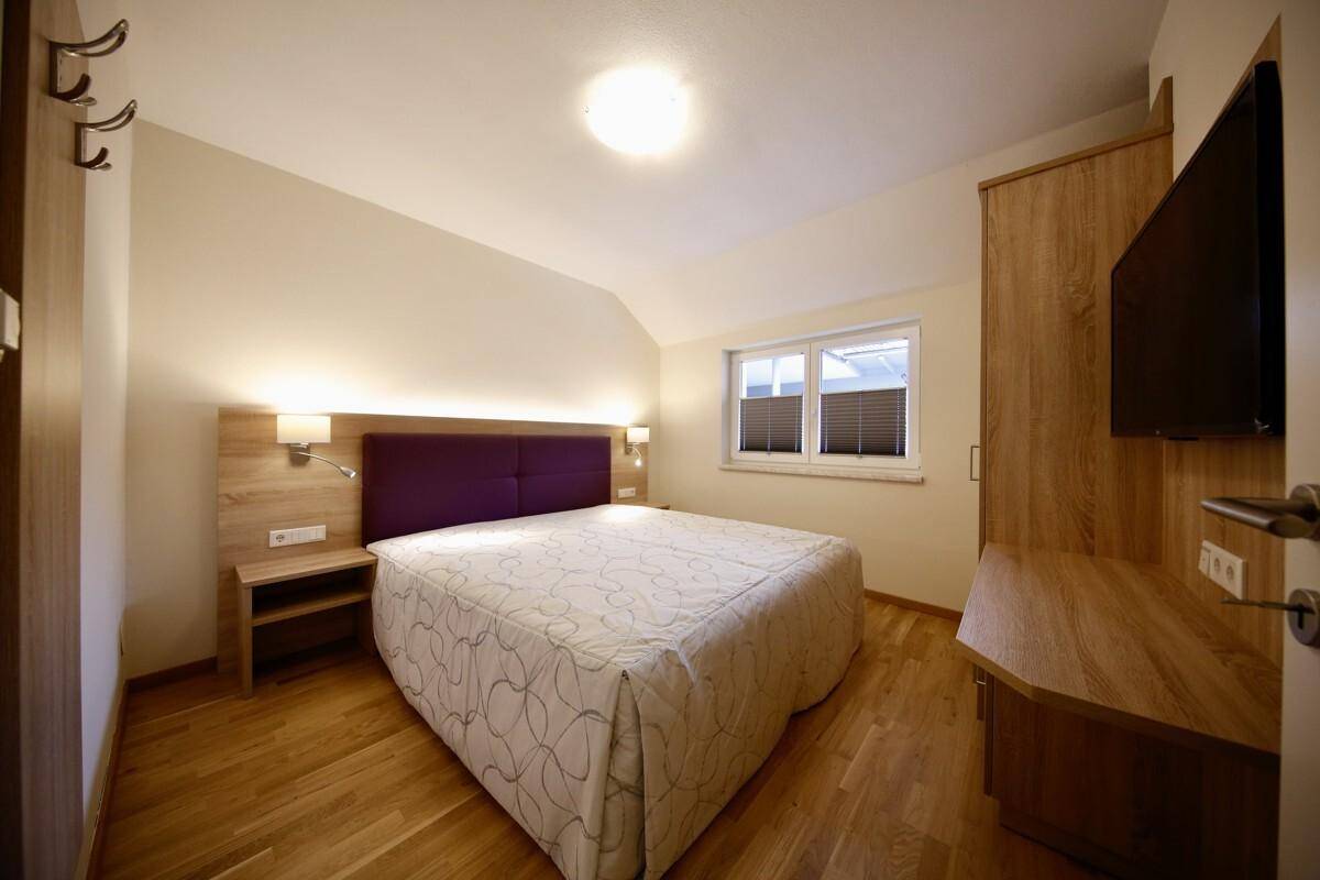 Schlafzimmer mit Doppelbett, Holzmöbeln und einem Fenster mit dunklen Jalousien für Privatsphäre.