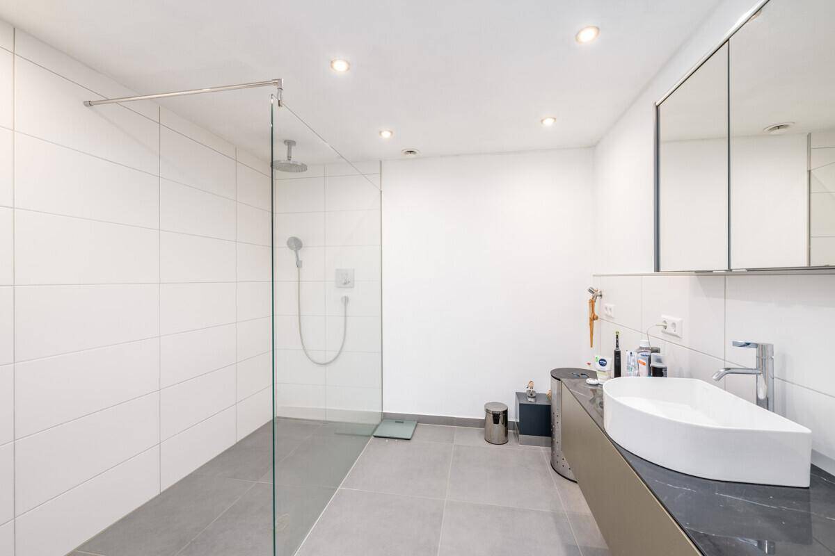 Modernes Badezimmer mit ebenerdiger Dusche, großem Waschbecken und Spiegelschrank.