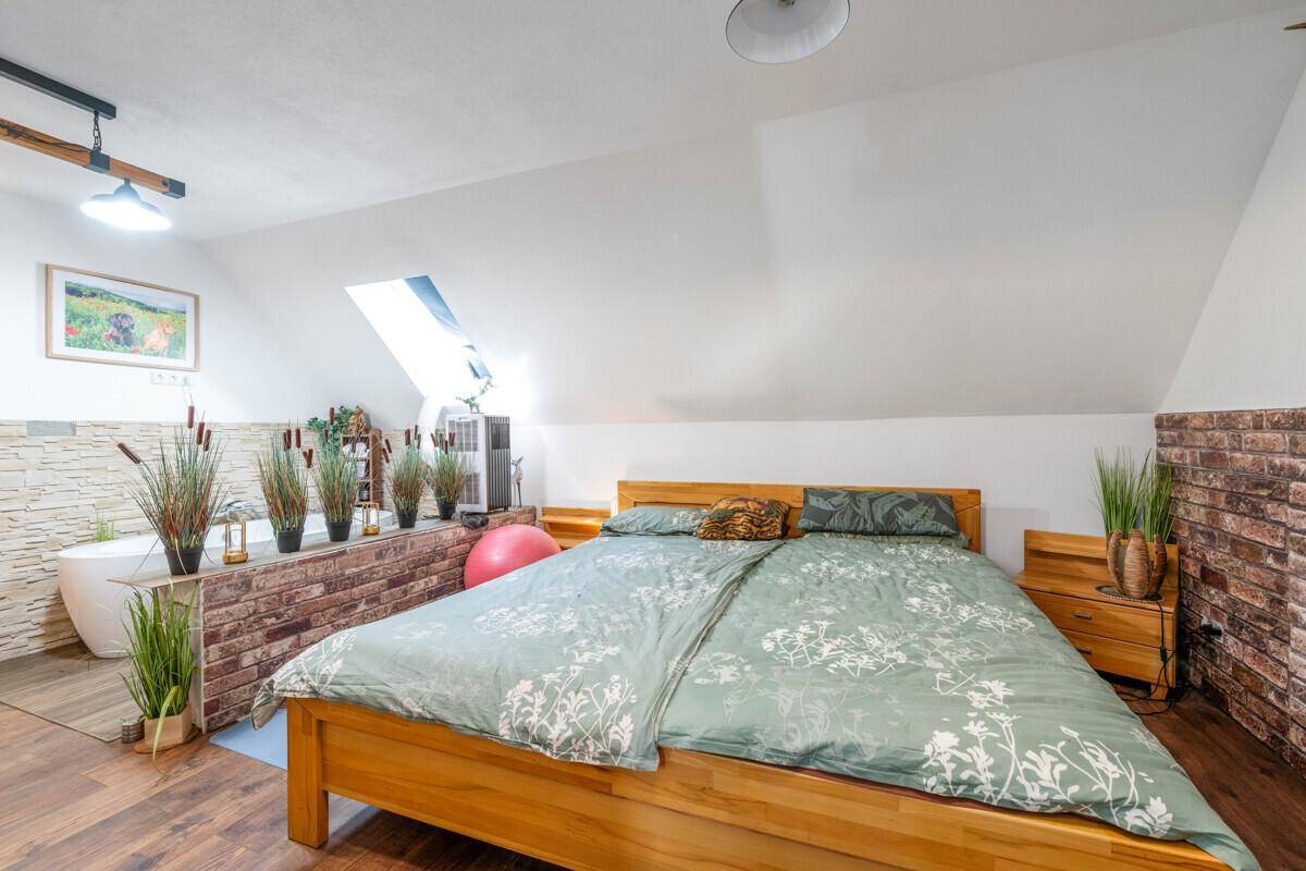 Schlafzimmer mit Holzbett und einer freistehenden Badewanne im offenen Bereich unter der Dachschräge.