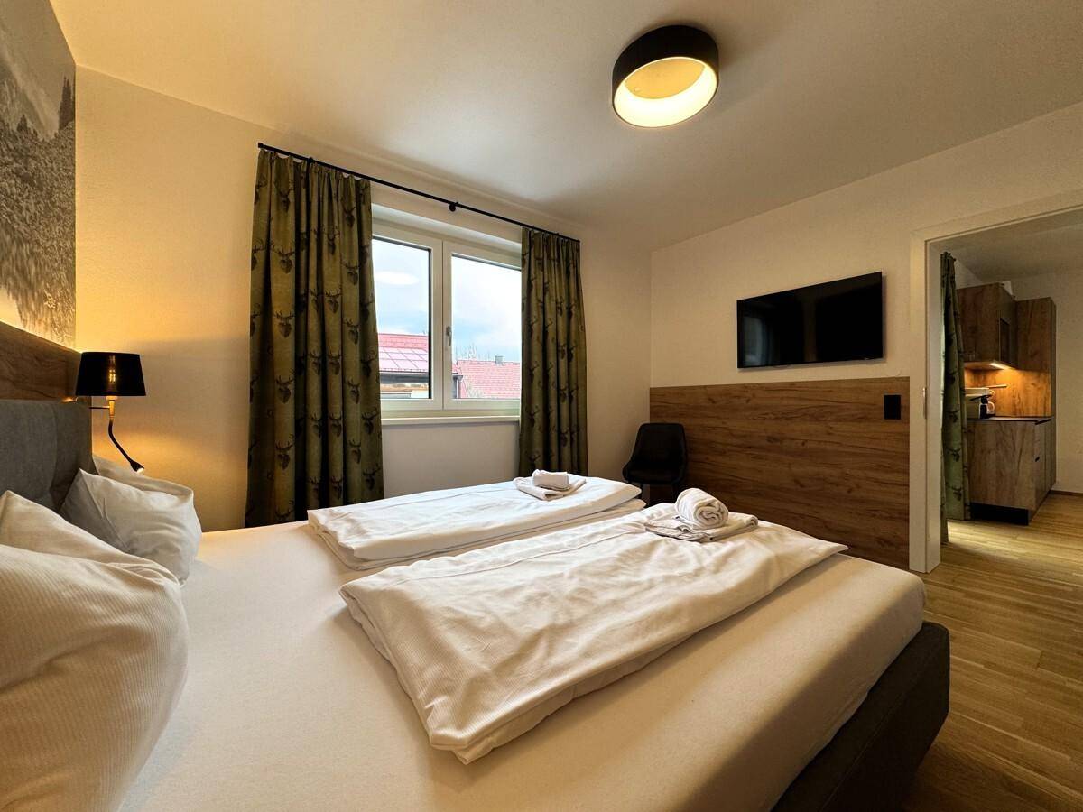 Schlafzimmer mit Doppelbett, Fernseher und Zugang zu einer kleinen Küchenzeile.