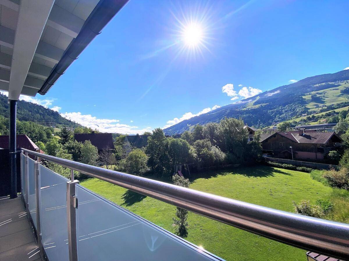 Sonniger Balkon mit Glasgeländer und herrlichem Blick auf die grüne Berglandschaft.