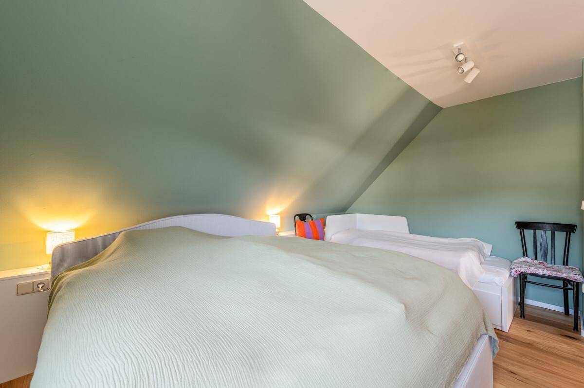 Gemütliches Schlafzimmer mit grünen Wänden, Holzboden und Dachschräge.