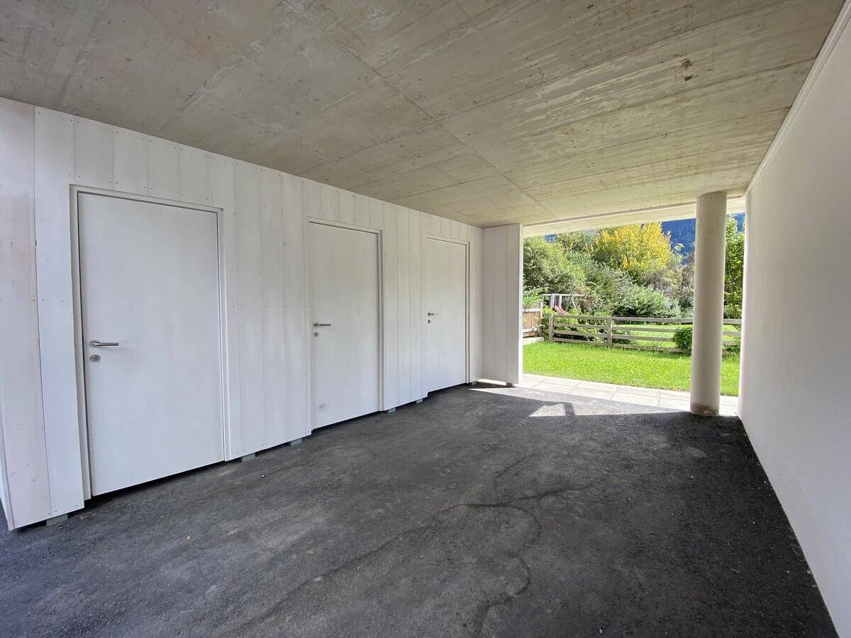 Geräumiger Carport mit Abstellräumen und Zugang zum grünen Außenbereich.