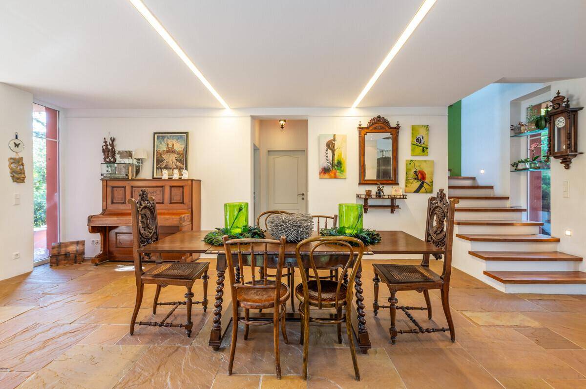 Eleganter Essbereich mit großem Holztisch, Stühlen und einem Klavier, angrenzend an eine Treppe.