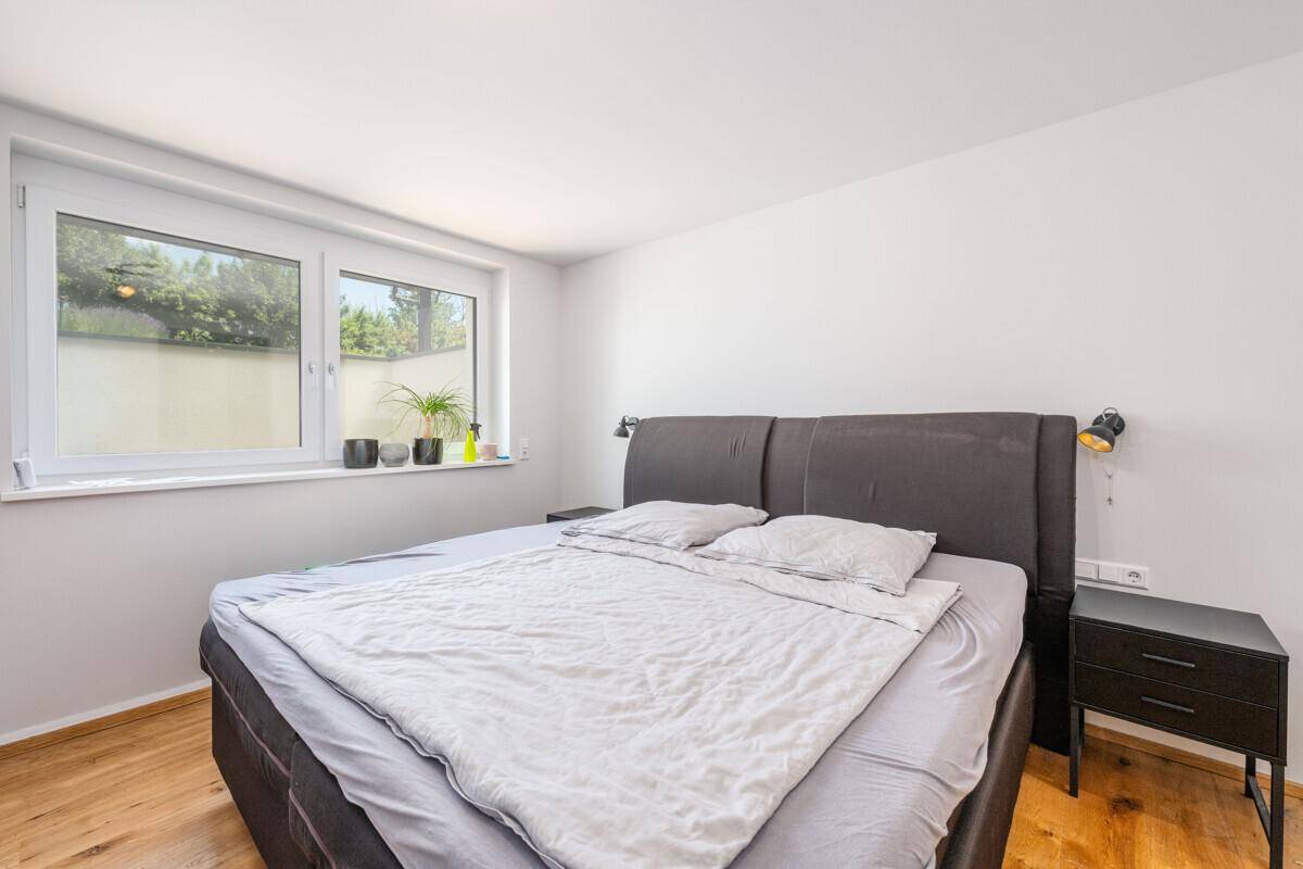 Modernes Schlafzimmer mit Doppelbett, Holzboden und großem Fenster mit Blick ins Grüne.