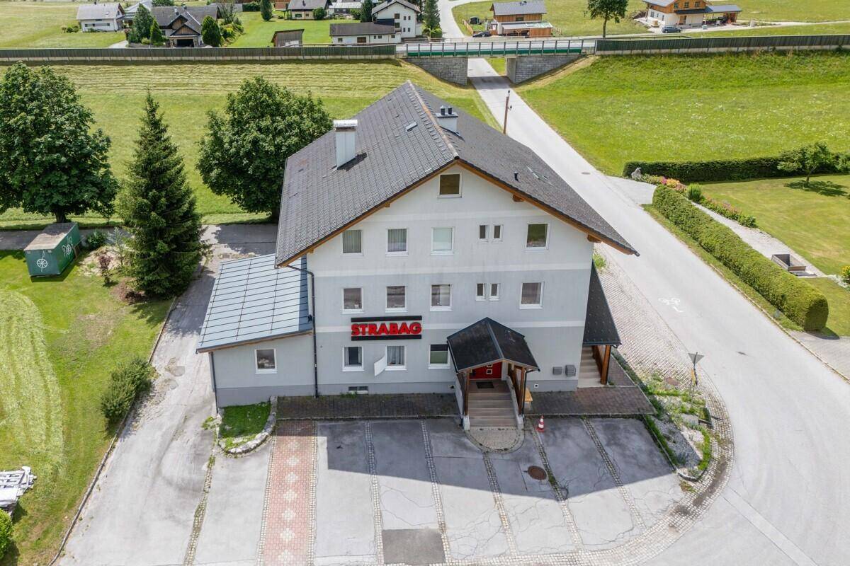 Luftaufnahme des Gebäudes mit Parkplätzen und grüner Umgebung, umgeben von Bergen.