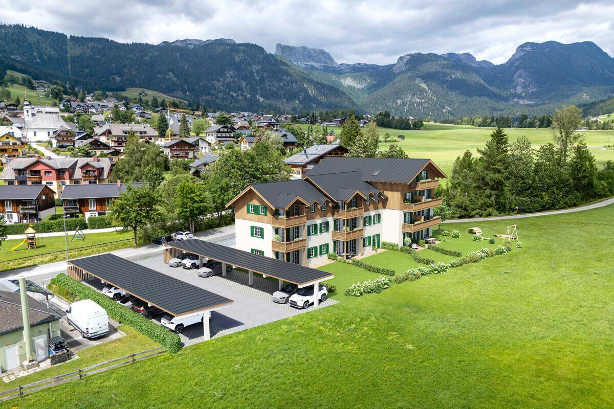Luftaufnahme einer modernen Wohnanlage im Alpenstil mit Carports und weitläufiger Grünfläche.