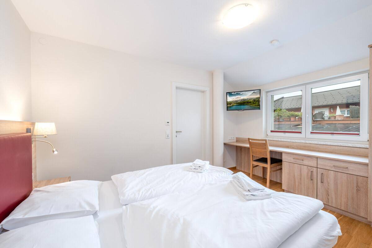 Helles Schlafzimmer mit Doppelbett, Schreibtisch und Fenster, das viel Tageslicht hereinlässt.