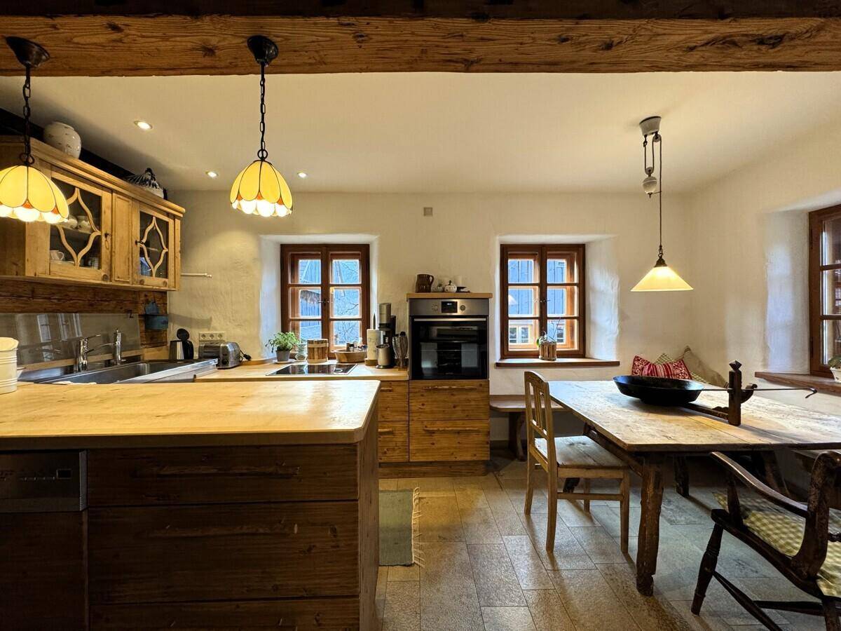 Funktionale Wohnküche mit Holzschränken, Spülbecken und Esstisch, unter einer rustikalen Holzbalkendecke.