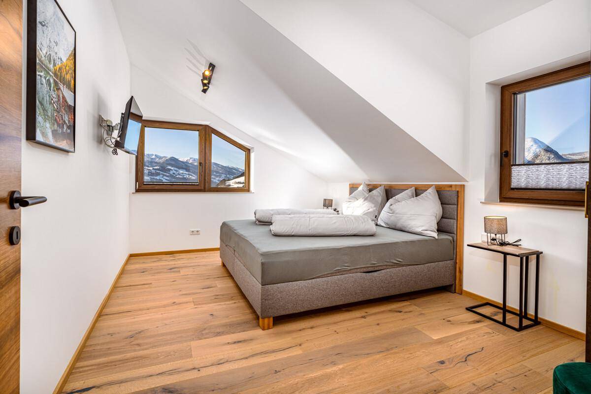 Helles Schlafzimmer mit Holzboden, Dachschräge und zwei Fenstern mit Bergblick.