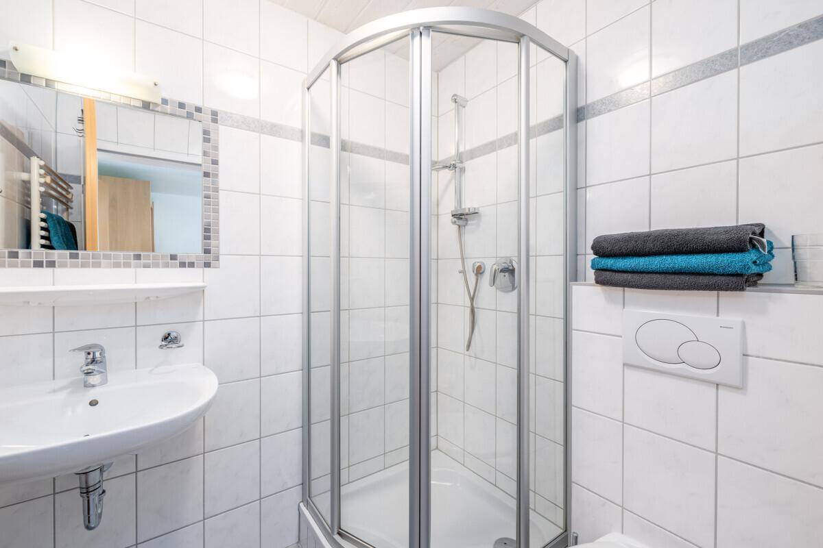 Badezimmer mit Eckdusche, weißen Fliesen und einem einzelnen Waschbecken, hell und funktional.