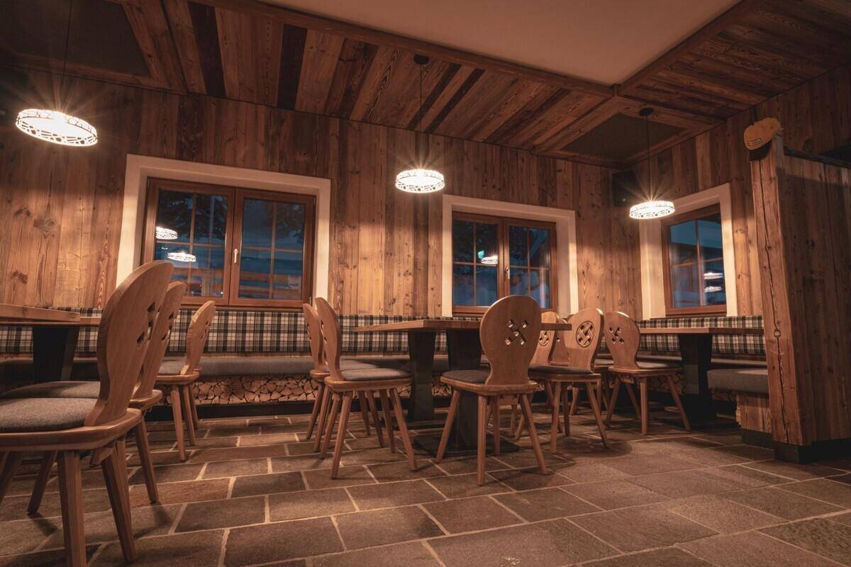 Gemütlicher Speisesaal im alpinen Stil mit Holztäfelung, karierten Sitzbänken und warmem Licht.