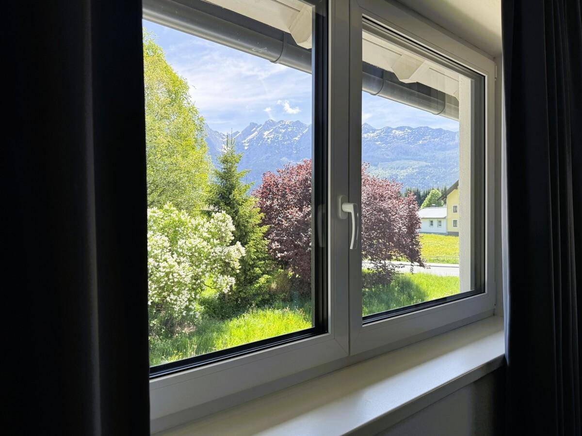 Fensterblick auf grüne Landschaft und Berge, mit viel Tageslicht.