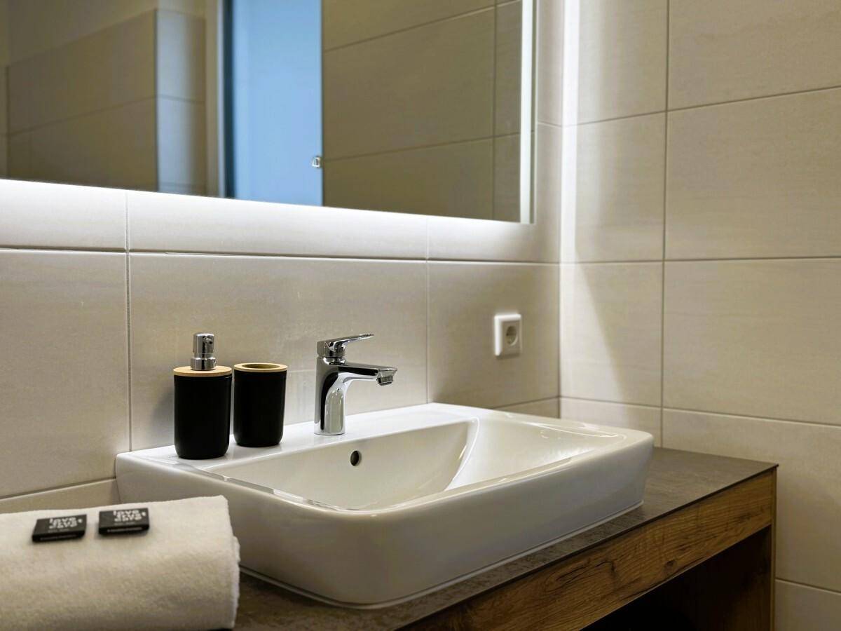 Modernes Badezimmer mit Aufsatzwaschbecken, beleuchtetem Spiegel und hellen Fliesen.
